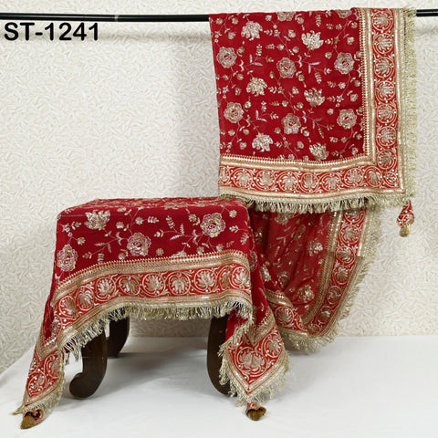 a red and gold tablecloth with intricate floral designs, hanging on a rod.
