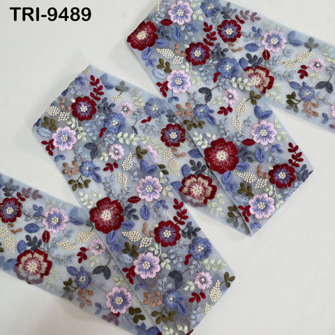 a close-up view of a fabric with a floral pattern, featuring various shades of blue, red, and white flowers and leaves. The fabric appears to be a piece of embroidered material, with the intricate details and vibrant colors creating a visually appealing design.