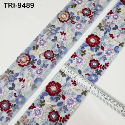a pair of fabric pieces with a floral embroidered pattern on them. The fabric pieces are placed next to a ruler, which is used to measure the length of the fabric.