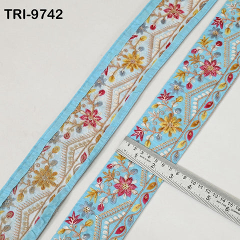 a close-up view of a decorative fabric with a floral pattern in shades of blue and gold. A ruler is placed on the fabric, indicating its size.
