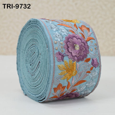 A roll of blue fabric with a floral embroidered design, featuring a large purple flower and smaller flowers in shades of orange and yellow.