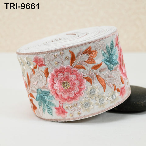 A decorative floral embroidered fabric, featuring a large pink flower surrounded by smaller flowers and leaves in various colors.