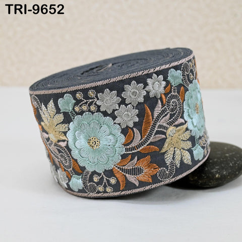 a decorative fabric with a floral pattern, including various shades of blue, green, and orange flowers, as well as leaves and other natural elements. The fabric appears to be a decorative trim or border, with the text "TRI-9652" visible in the image.