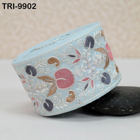 A roll of embroidered fabric with a floral pattern, placed on a black rock.