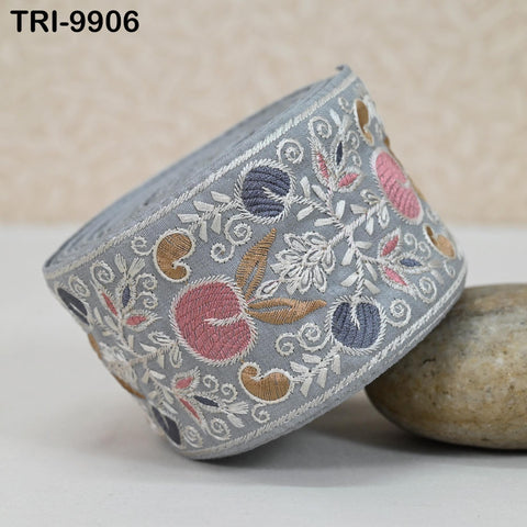 a decorative gray fabric with intricate floral embroidery, including pink and blue flowers, placed on a white surface.