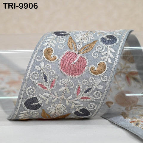 a decorative fabric with a floral pattern, including a large red flower surrounded by smaller flowers and leaves. The fabric appears to be a decorative trim or border, with intricate embroidered designs.