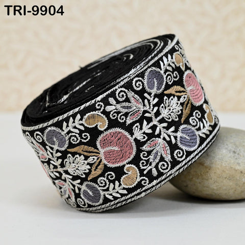 a decorative black and white fabric with a floral pattern, including pink and purple flowers, and gold and white floral elements. The fabric is rolled up and placed on a surface, with a rock nearby.
