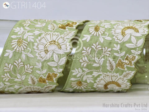 a close-up view of a decorative fabric with a floral pattern in shades of green and white, adorned with gold sequins and beads.