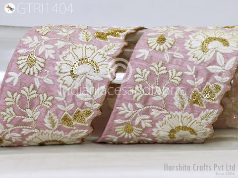 a close-up view of a decorative fabric with a floral pattern in shades of pink and white, adorned with gold sequins and beads.
