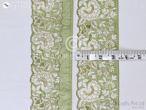 a close-up view of a decorative fabric with a floral pattern in shades of green and white. The fabric appears to be made of a material with a scalloped edge, and there is a ruler placed next to it, indicating the size of the fabric.
