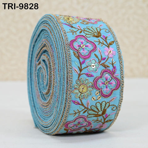 A roll of blue fabric with a floral pattern and gold embroidery.