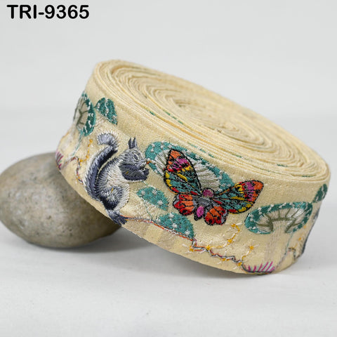 A beige fabric with a colorful butterfly and a squirrel embroidered on it, along with other small embroidered designs.