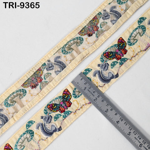 a decorative fabric with a repeating pattern of butterflies and other floral designs. A ruler is placed on the fabric, indicating the size or dimensions of the pattern.