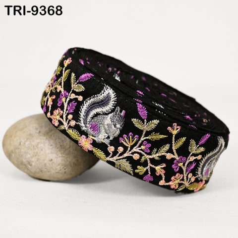 A black and purple embroidered piece of fabric with a floral pattern, resting on a gray rock.