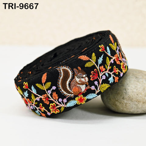 A black fabric with a colorful floral and leaf embroidered design, featuring a squirrel on the fabric.