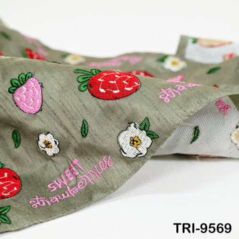 a close-up view of a fabric with a repeating pattern of strawberries and flowers, including white flowers and green leaves. The fabric appears to be a light green color, and the embroidered design is visible.