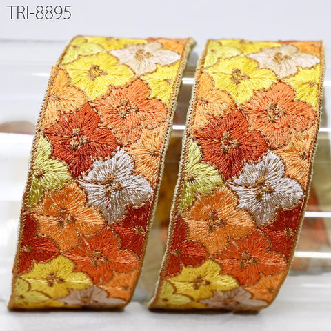 a decorative ribbon with a floral pattern in shades of yellow, orange, and white. The ribbon appears to be made of embroidered material and is displayed against a white background.