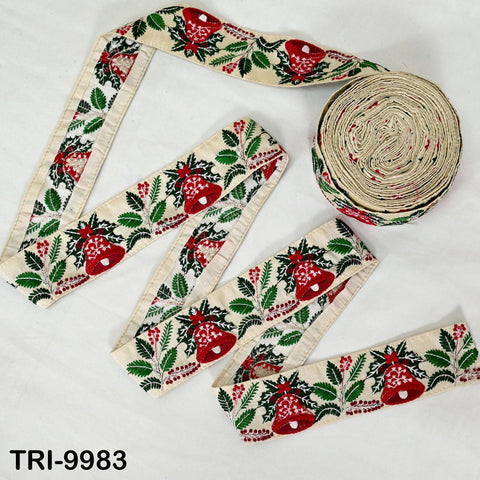 a spool of embroidered fabric with a repeating pattern of red berries, green leaves, and white flowers. The fabric appears to be a decorative trim or ribbon, and there is a round object resembling a ribbon or ribbon holder in the background.