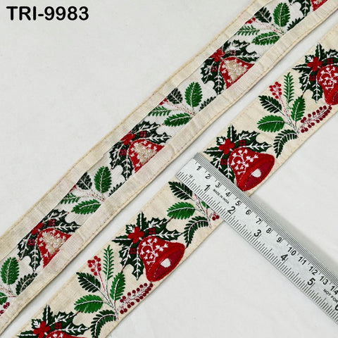 a decorative fabric with a repeating pattern of red and green leaves and red bells, laid out on a white surface. A ruler is placed next to the fabric, indicating the size of the pattern.