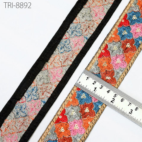 a close-up view of a decorative fabric with a floral pattern, featuring a black border and a ruler for size reference.