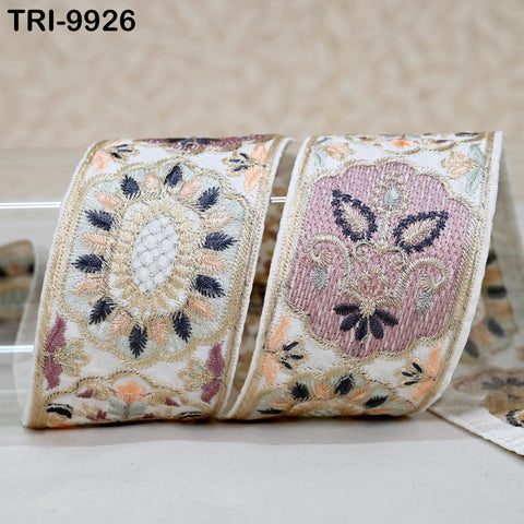 two decorative fabric pieces with intricate embroidered patterns in shades of pink, white, and blue. The pieces are placed on a white surface, and there is a blurred background.