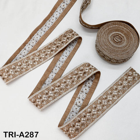 a collection of decorative fabric pieces, including a spool of brown and white embroidered ribbon and several pieces of fabric with intricate patterns.
