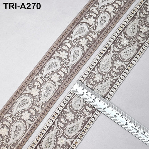 a close-up view of a decorative fabric with a repeating paisley pattern in shades of brown and white. The fabric appears to be a decorative trim or lace, with a ruler placed on it to provide a sense of scale.