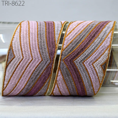 a decorative fabric with a striped pattern in shades of pink, purple, and orange. The fabric appears to be a decorative trim or ribbon, and it is placed on a surface.