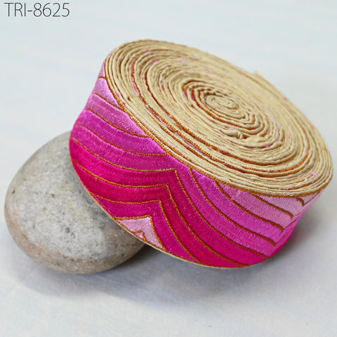 a close-up view of a decorative fabric with a pink and gold pattern, resting on a gray rock.