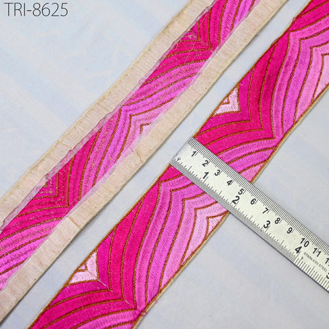a close-up view of a pink and gold patterned fabric, with a ruler placed on top of it to measure its dimensions.
