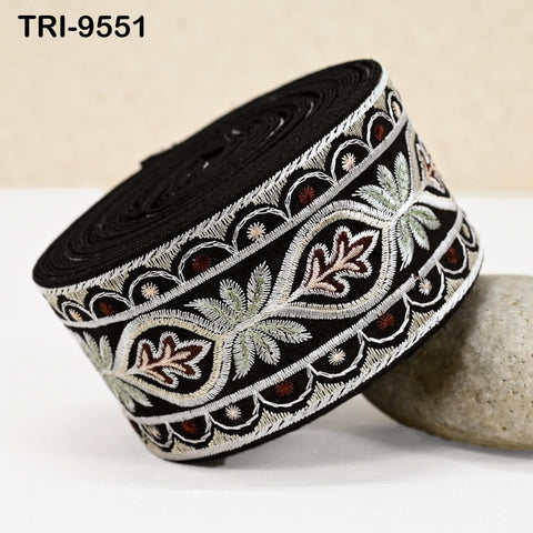 A close-up image of a decorative black and white fabric with intricate embroidered patterns, including leaves and flowers, resting on a white surface.