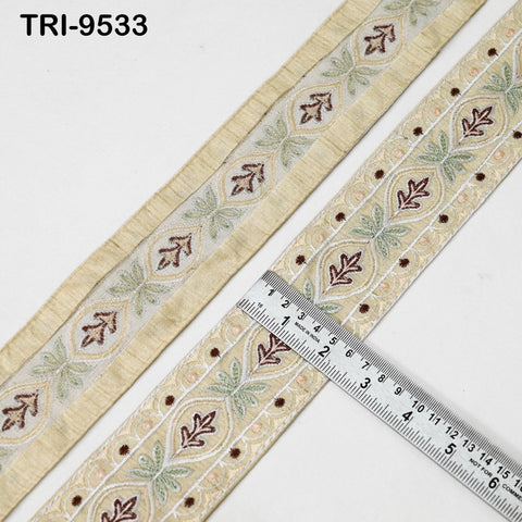 a decorative beige fabric with a repeating pattern of floral and leaf designs, and a ruler placed on top of it to measure its length.