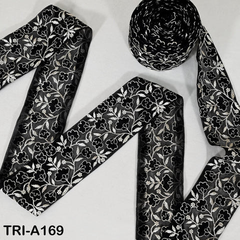 a black and white floral patterned fabric, which appears to be a decorative textile or ribbon. The fabric is rolled up and placed on a white surface, creating a visually striking contrast between the black and white colors.