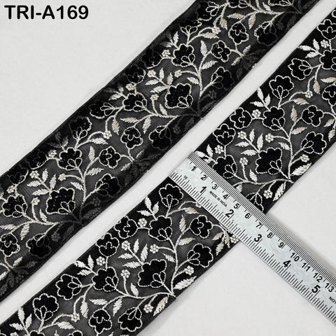 a close-up view of a black and white floral embroidered fabric, with a ruler placed on top of it to measure its length.