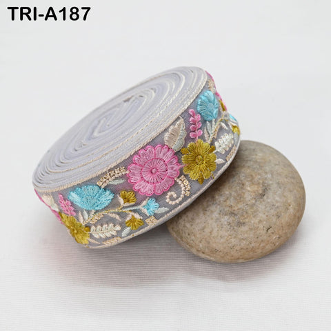 a decorative fabric with a floral pattern, including pink, blue, and yellow flowers, and a gray circular object with a floral design on it, placed on a white surface.
