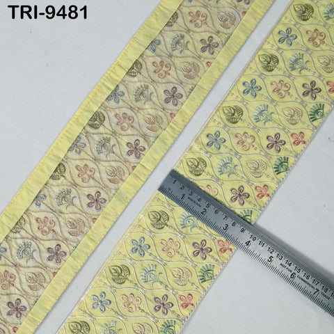 two pieces of fabric with a repeating floral pattern in yellow and green colors. A ruler is placed on top of one of the fabric pieces, indicating the size or dimensions of the fabric.