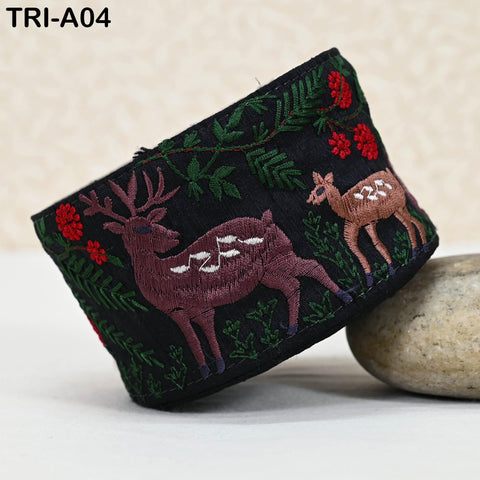 a black fabric with a decorative embroidered design of deer and red flowers.