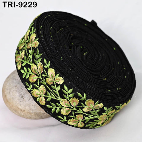 a black fabric with a floral embroidered border, featuring green and yellow flowers. The fabric appears to be rolled up and placed on a white surface.