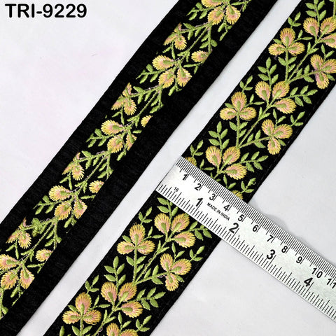 a close-up view of a decorative black and yellow embroidered fabric, with a ruler placed on top of it to measure its length.