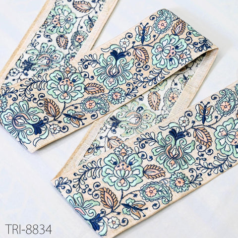 a decorative fabric with a floral pattern in shades of blue, green, and orange. The fabric appears to be a piece of cloth or textile with a repeating floral design.