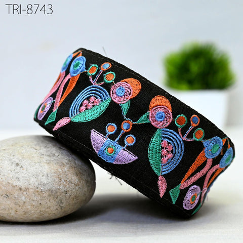 a black, colorful, and intricately embroidered headband or bracelet, resting on a white surface. In the background, there is a potted plant, adding a touch of greenery to the scene.