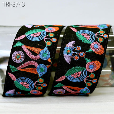 two decorative fabric pieces with a colorful, intricate embroidered pattern. The pieces appear to be black in color and feature a variety of shapes and designs, including flowers, leaves, and other abstract elements. The image does not contain any text or other discernible objects, and the focus is solely on the embroidered patterns.