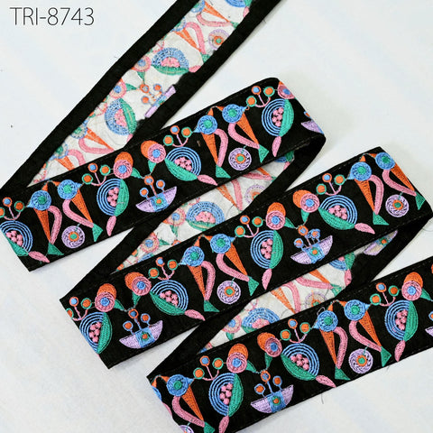 a decorative fabric with a repeating pattern of colorful flowers and leaves in various shades of pink, blue, green, and orange. The fabric appears to be a decorative trim or border, and it is displayed on a white surface.