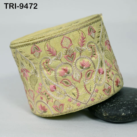 a decorative yellow fabric with a floral pattern, including pink and green flowers, and leaves. The fabric appears to be a piece of clothing or accessory with a detailed embroidered design.