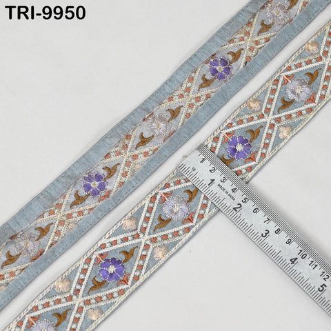 a decorative fabric with a repeating pattern of flowers and geometric shapes in shades of blue, gray, and brown. A ruler is placed on the fabric, indicating the size of the pattern.