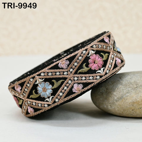 A decorative black and pink embroidered band with a floral pattern rests on a rock.