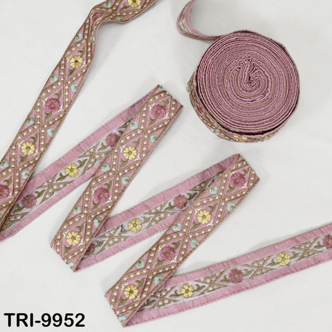 a collection of decorative fabric pieces, including a spool of pink and green embroidered fabric and several pieces of fabric with intricate floral patterns.