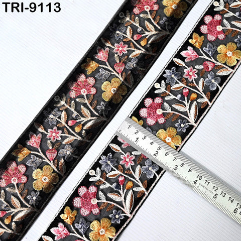 a close-up view of a decorative floral embroidery ribbon with a ruler placed next to it, indicating the ribbon's size.