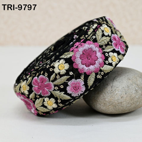A decorative black and pink embroidered fabric with floral patterns, resting on a gray rock.
