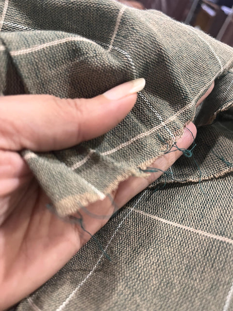 A close-up view of a hand holding a piece of fabric with a green and white pattern, showing the fabric's texture and the person's fingers.